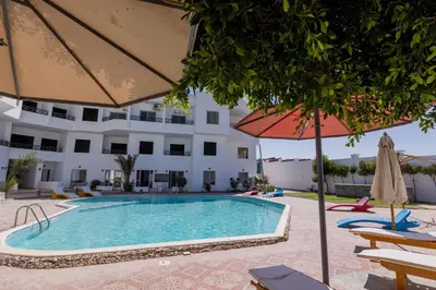 a swimming pool with an umbrella and chairs and a building at La bonita compound in Hurghada