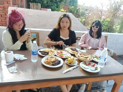 three women sitting at a table eating food at ABU Nubian Guest House in Aswan