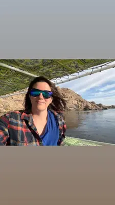 a woman in sunglasses sitting on a boat on the water at Felucca sailing overnight experience with imaginative felucca aswan in Aswan