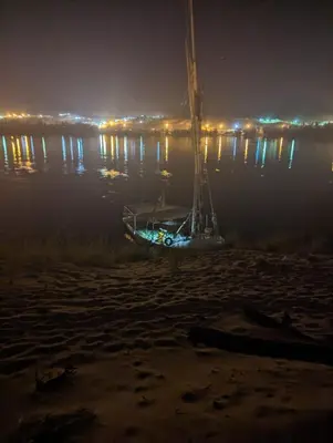 a boat sitting on the shore of the water at night at Felucca sailing overnight experience with imaginative felucca aswan in Aswan