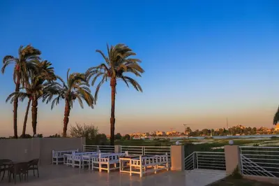 a patio with tables and chairs and palm trees at Royal Nile Villas - Luxury Nile View Apartment 2 in Luxor