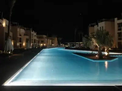 a large blue swimming pool at night with buildings at Mangroovy Magic PoolView 1BR in Beachfront Complex M3 3A 13 in Hurghada