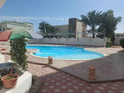 a large swimming pool with an umbrella in a courtyard at Makramia A107 studio in Hurghada