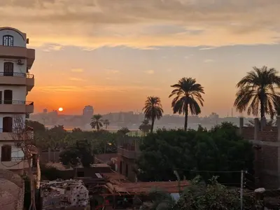a sunset over a city with palm trees and a building at Djorf apartments in Al Aqālitah