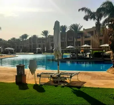 a umbrella and a chair next to a swimming pool at Шале Stella di mare Makadi Хургада in Hurghada