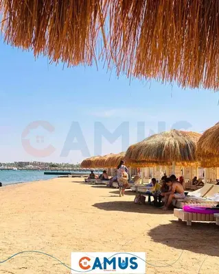 a beach with straw umbrellas and people sitting on the beach at CAMUS 343, Princess Resort in Hurghada
