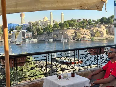 a man sitting on a balcony with a view of the river at Bakar Nubian Guest House in Aswan