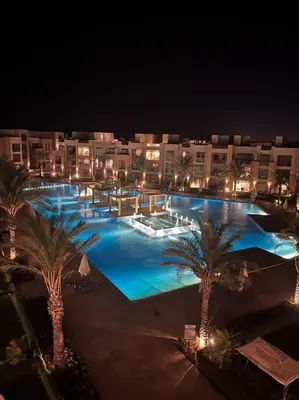 a large pool with palm trees and buildings at night at Mangroovy - Divine 1BR Hotel view in Hurghada