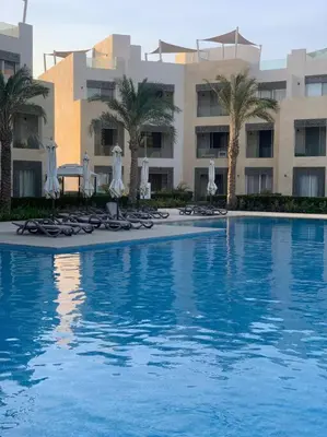a swimming pool with chairs and umbrellas and a building at Mangroovy - Divine 1BR Hotel view in Hurghada