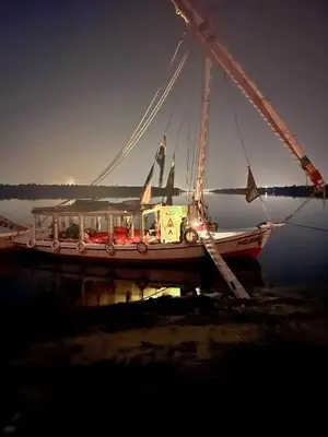 a boat sitting in the water with its lights on at Aswan Felucca sailing boat and Hotel in Aswan