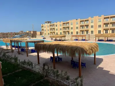 a resort with a table and straw umbrellas and a swimming pool at Bay View Sahl hasheesh Apartment Hurghada in Hurghada