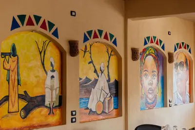 a group of paintings on the wall of a room at ACHERTOD Nubian House in Naj‘ al Maḩaţţah