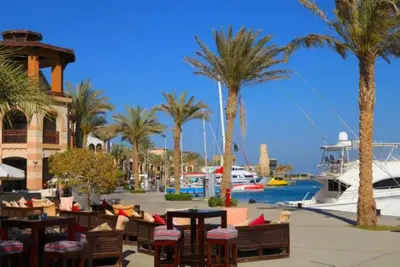 a resort with palm trees and tables and a boat at FeWo Port Ghalib in Port Ghalib
