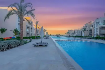 a resort swimming pool with a sunset in the background at Beach-Inspired 1BR in Mangroovy, El Gouna. Sea & Pool in Hurghada
