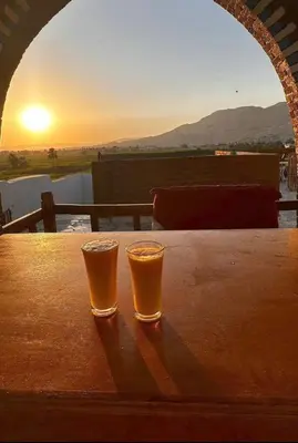 two glasses of beer sitting on a table with the sunset at Quiet Gate Guest House in Al Aqālitah