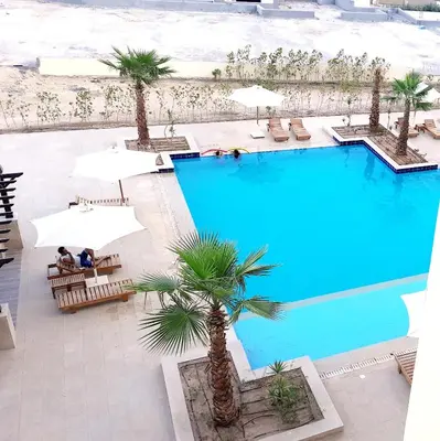 an overhead view of a swimming pool with palm trees and umbrellas at AlDau heights Maher in Hurghada