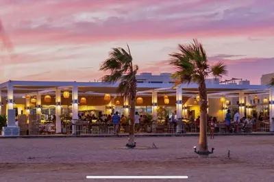 a restaurant on the beach with palm trees in front at Cozy 1 Bedroom Ground Floor Apartment with Pool in Hurghada