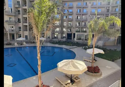 a swimming pool with umbrellas and palm trees in front of a building at Princess resort in Hurghada