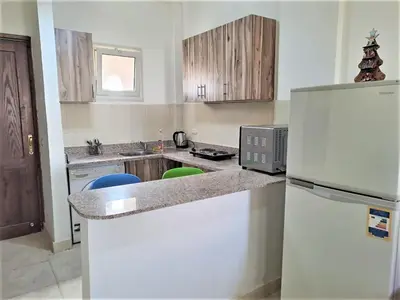 a kitchen with a white refrigerator and wooden cabinets at 2 bedroom modern flat at Makadi heights in Hurghada