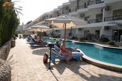 a person sitting on a bench next to a swimming pool at FOX SAHEL AQUA RESORT ELGOUNa& Kite in Hurghada