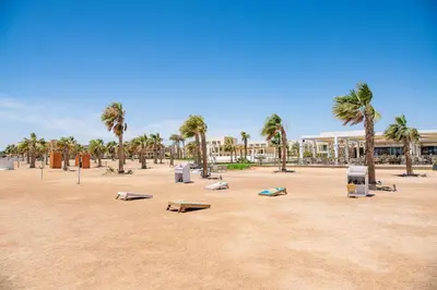 a park with benches and palm trees and a building at Cozy 1BR Apartment in Mangroovy with pool in Hurghada