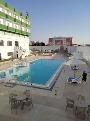 a swimming pool with tables and chairs and a building at Badr Hotel & Resort El Kharga in Kharga