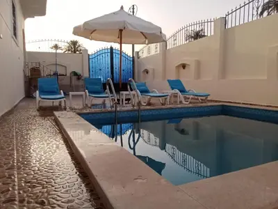 a swimming pool with chairs and an umbrella at Nille and Garden View Apartment in Jazīrat al ‘Awwāmīyah