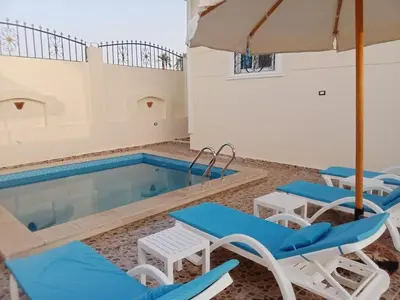 a pool with chairs and an umbrella and a swimming pool at Nille and Garden View Apartment in Jazīrat al ‘Awwāmīyah