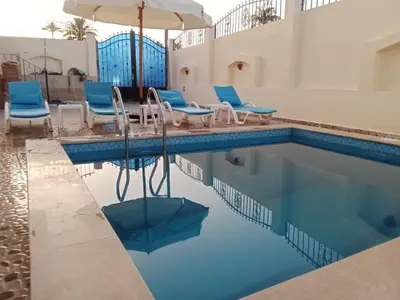 a swimming pool with blue chairs and an umbrella at Nille and Garden View Apartment in Jazīrat al ‘Awwāmīyah