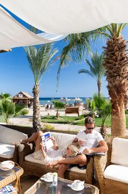 a man and a woman sitting on a chair on the beach at Three Corners Equinox Beach Resort in Abu Dabab
