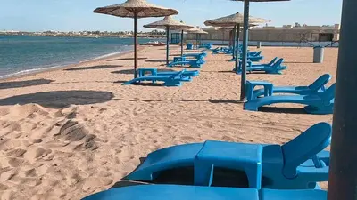 a beach with blue lounge chairs and umbrellas at Apartment in Cecelia Resort in Hurghada