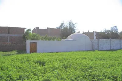 a white building in a field next to a fence at Happy house in Luxor