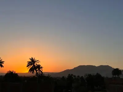 a sunset with palm trees and a mountain in the background at Luxor Sun Villa in Luxor