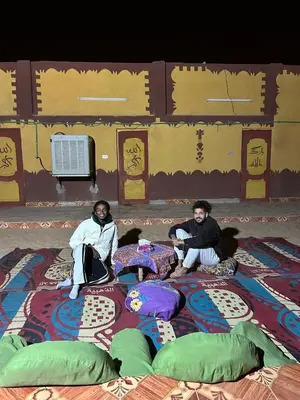 two people sitting on a rug on the ground at Bafana Bafana Nubian Hostel in Najâ€˜ al MadÄbb