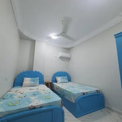 two beds in a room with blue chairs at Lareen's apartment in Quseir