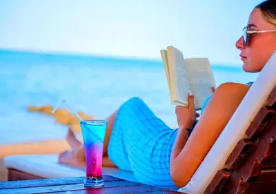 a woman laying on a table reading a book and a drink at Davinci Beach Resort in Hurghada