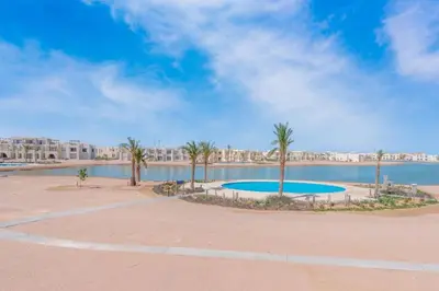 a pool with palm trees next to a body of water at Sunny 1BR Retreat Newest Project Shedwan El Gouna Lagoon & Pool in Hurghada