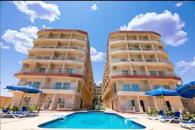 two tall apartment buildings with a swimming pool and blue umbrellas at Casablanca Beach hurgada كازابلانكا بيتش الغردقه in Hurghada