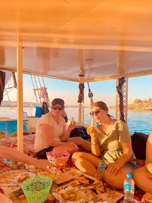 three women sitting on the back of a boat at Felucca sailing boat from Aswan to komombo with private bathroom in Aswan