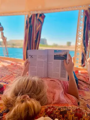a little girl laying on a bed reading a book at Felucca sailing boat from Aswan to komombo with private bathroom in Aswan