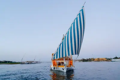 a small boat with a blue and white sail on the water at Turquoise Dahabiya , 3,4,7 nights sailing between Luxor and Aswan in Luxor