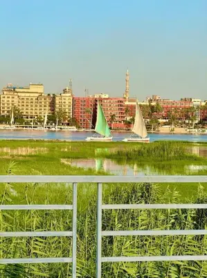two sailboats in a body of water next to a fence at Royal Nile Suites - Nile View 1 in Luxor