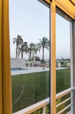 a window with a view of a yard with palm trees at Royal Nile Suites - Luxury Nile View 1 in Al Aqālitah