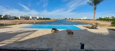 a swimming pool with two chairs next to a body of water at Joubal lagoon Elgouna 2BD in Hurghada