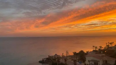 a sunset over the ocean with palm trees and houses at Luxurious and Cozy Seafront Studio Near Gouna in Hurghada