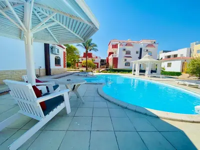 a swimming pool with a white umbrella and a table and chairs at Magawish villa in the heart of the city in Hurghada