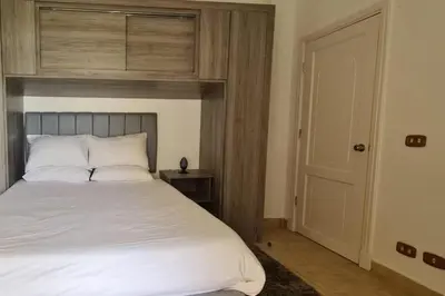 a bedroom with a white bed with a wooden headboard at Nile Front Luxor Apt Sleeps 6 with Pool in Luxor