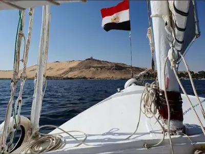 a boat in the water with a mountain in the background at شقق للإيجار بأسوان in Aswan