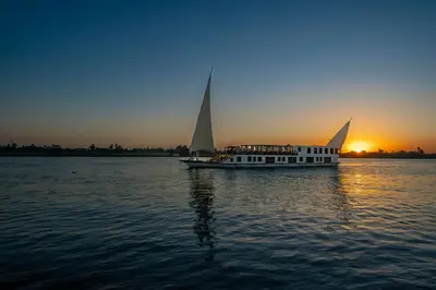 a boat with sails in the water at sunset at Princess Farida Luxury Dahabiya Nile Cruise, Every Monday from Luxor to Aswan 4 nights and Every Friday from Aswan to Luxor 3 nights in Luxor