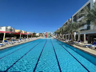 a swimming pool with chairs and palm trees and buildings at Fanadir bay resort in Hurghada